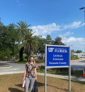 emma lonnberg, an intern at uf/ifas extension sarasota county, stands outside in front of an office sign.