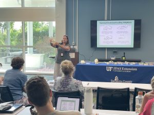 An image of a woman holding up an animal skull teaching a room of adults.