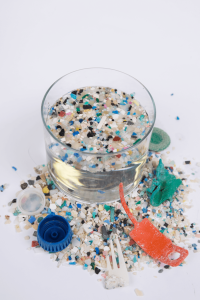 assorted microplastics shown in a clear, water-filled container, with a pile of microplastics at the base of the container. [credit: uf/ifas, tyler jones]