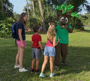 Woman and two children saying hello to a tree mascot.