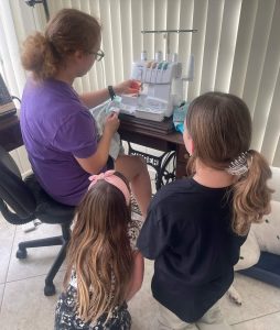 Ashley works on a sewing machine while two students look on. 