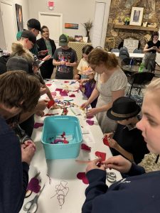 A group children gather around a table and learn how to hand-sew.