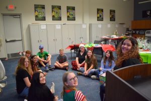A group of kids sit on the floor and form a circle. They all have Christmas jammies on!