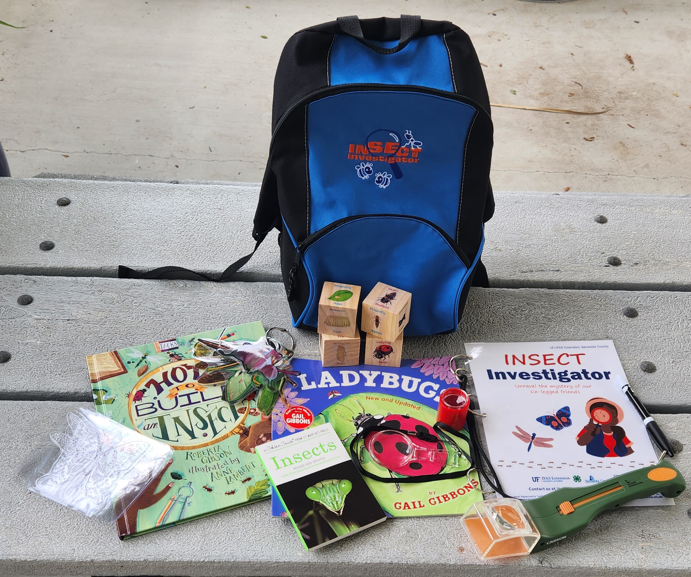 blue backpack surrounded by books, an insect catching device, and an insect life cycle game