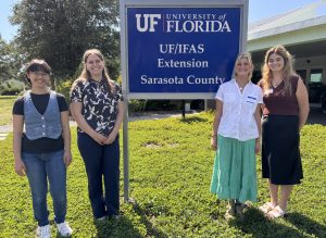 4 young women stand in a field with the office sign between them.