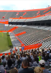 Kids sit in a football stadium's stands waiting for a tour to begin.