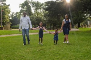 An image of parents and kids holding hands walking through a green park.