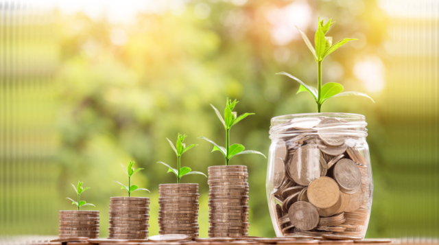 plant shoots sprout from stacks of coins and a clear glass jar full of coins, against a background of greenery. [credit: pixabay.com, nattanan kanchanaprat]