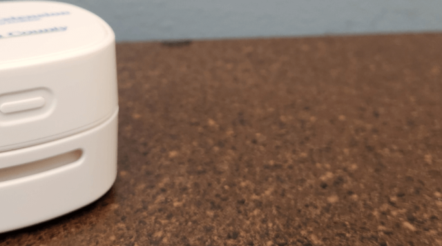 Crumb cleaner device on brown counter with blue wall in background (a crumb cleaner is a mini vacuum that cleans surfaces like counters)