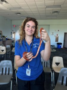 Intern Evelyn in a blue shirt holding an orange snake and smiling.