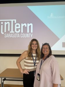 Evelyn standing with her supervisor in front of a screen that reads "Intern Sarasota County".