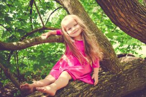 A young girl sitting barefoot in a tree.