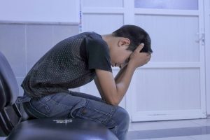 An image of a young boy crouched over, leaning his head into his hands sadly.