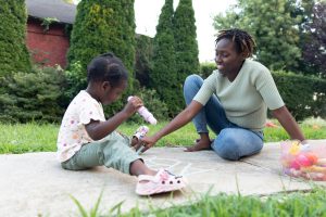 An image of a mother teaching a child writing with chalk on a sidewalk.