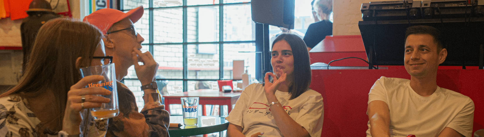 a group of young adults sits at a table in a restaurant/bar, with "brewing ideas" pint glasses, sharing conversation. [credit: unsplash.com]