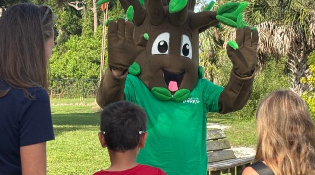 someone dressed as a tree out in a park with a family