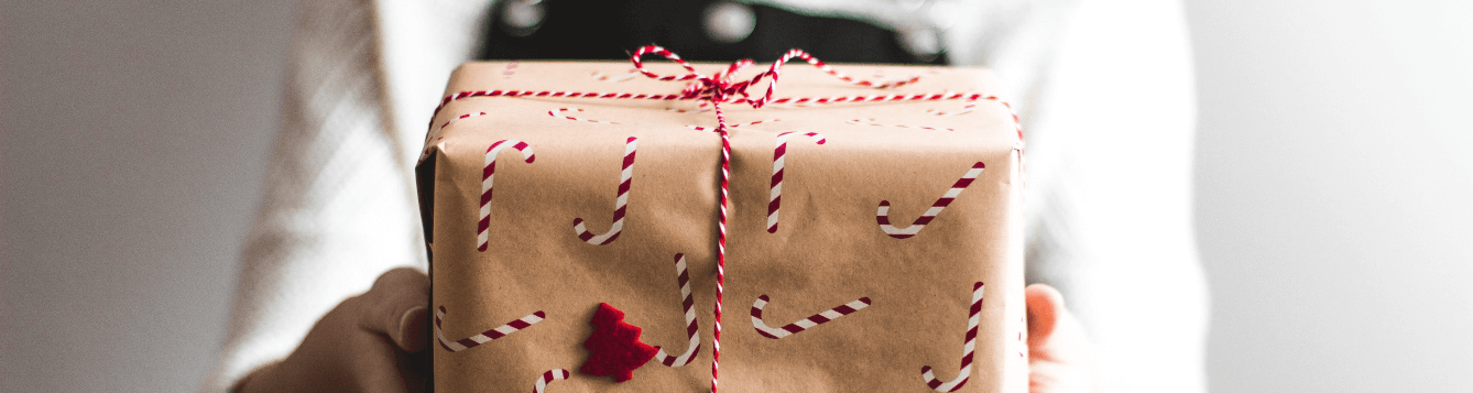 a person holds a personally wrapped holiday gift in two hands, sharing it to the viewer. [credit: unsplash.com, Kira auf der Heide]