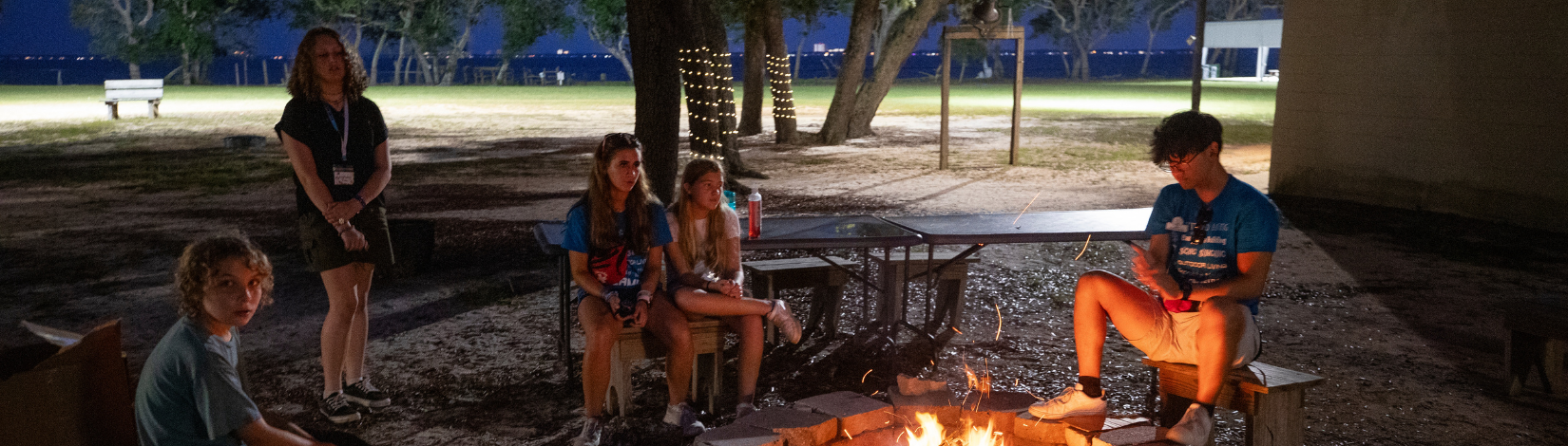 4-H'ers sit around a fireplace at night.