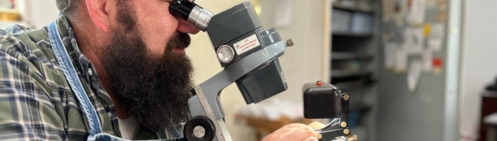 A man authenticates a diamond by looking through a microscope.