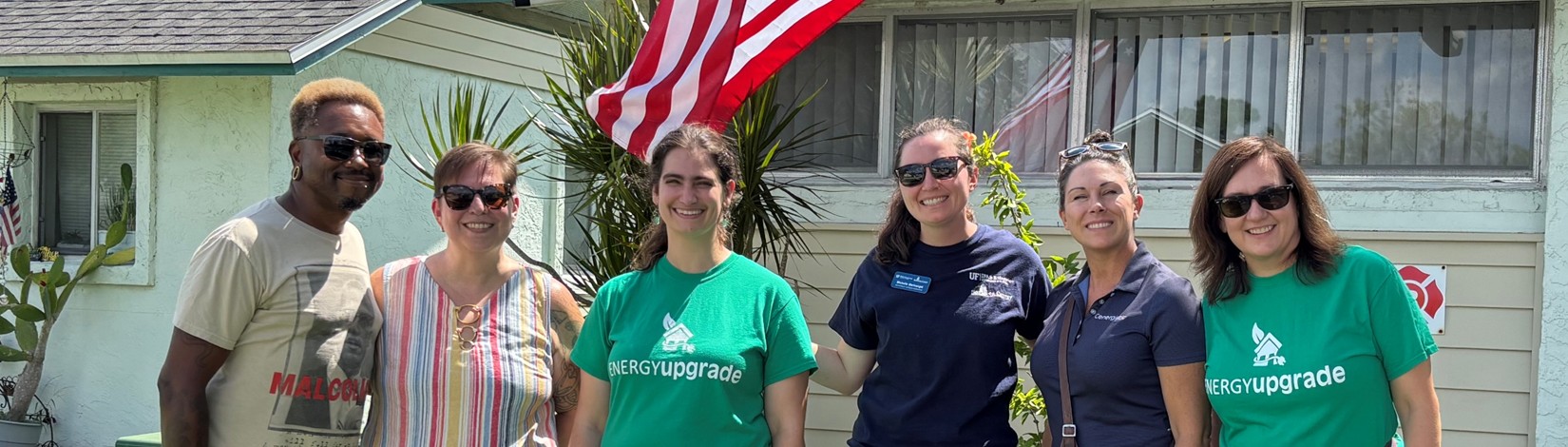 Six Energy Coaches stand smiling in front of an office with an American flag behind them.
