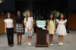 Picture of county five county 4-H Public Speaking winners. All are female standing in the front of the Board of County Commissioners Chamber