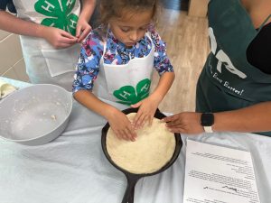 4-H youth making pizza dough in cast iron pan at county line camp
