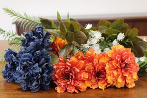 flowers stacked on a table in colors blue, orange, greenery with flowers and more greenery
