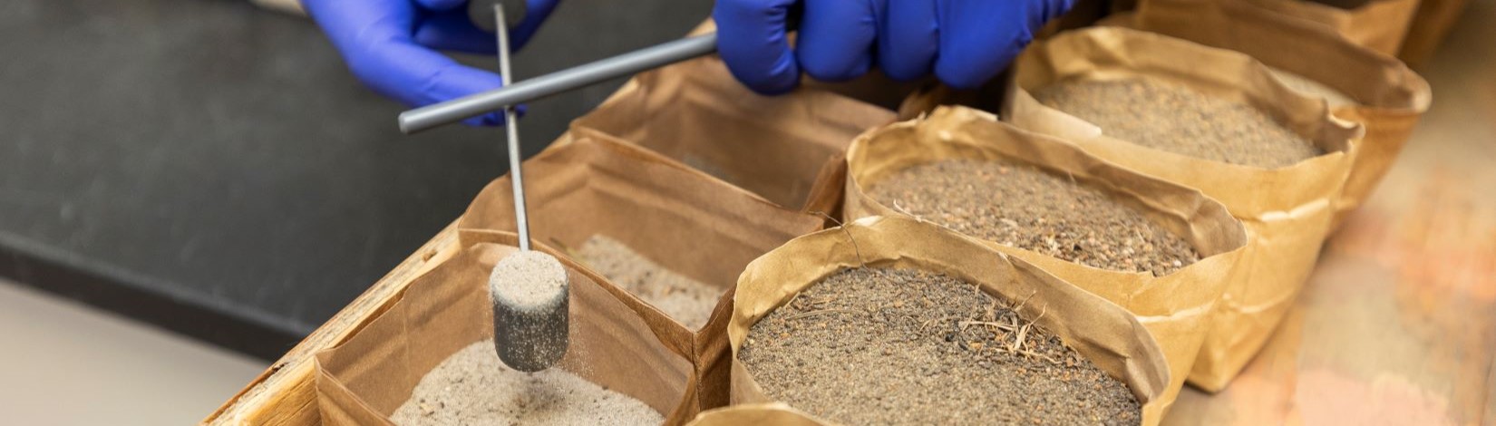 a person's hands scooping soil out of a brown paper sample bag.