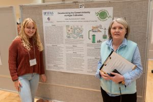 Two women standing at a bulletin board with a research poster hanging on it.