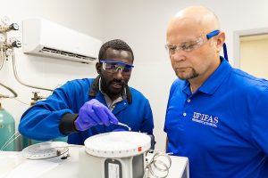 Two men in a lab stand over soil and water analytical equipment.