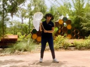 A college student stands outside of the Florida Botanical Gardens holding a butterfly net for a bug bioblitz event during her summer experience.