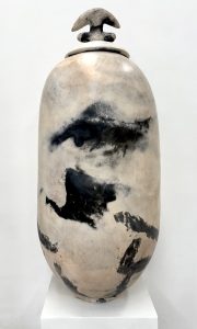 A tall, oval shaped vase with a lid on it with large, irregular black shapes after firing it in a barrel.