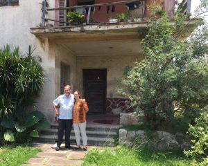 A man and woman stand in front of a two story house outside Havana, Cuba.