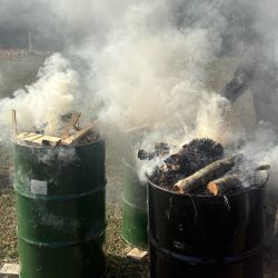 Gray smoke rises from two metal barrels during a ceramics firing.