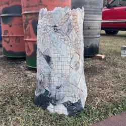 A tall ceramic cylinder that looks like a tree trunk stands in front of barrels used to fire art.