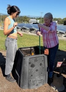 A professor shows a student how to turn compost in a bin.