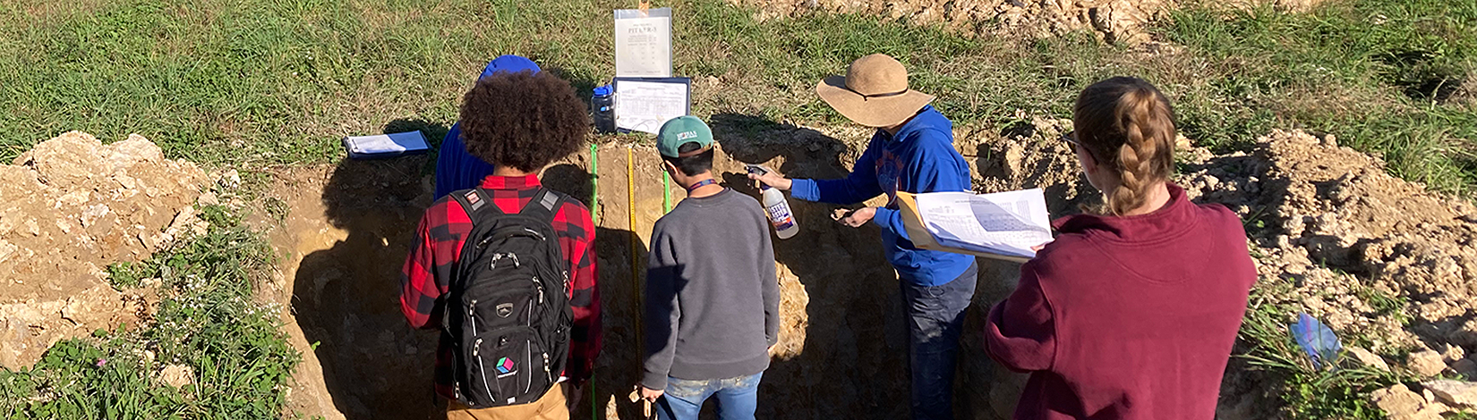 Five people on a soils judging team stand in a soil pit, analyzing the soil horizons.