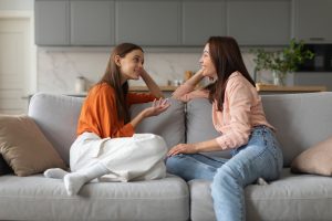 Loving mother listening to daughter with empathy and understanding, sitting together on sofa at home, parent communicating with teenager